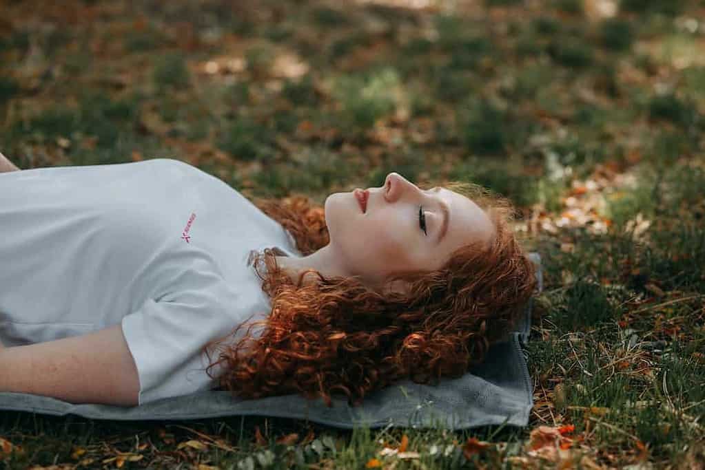 woman laying on her yoga mat in an outdoor scenary doing savasana