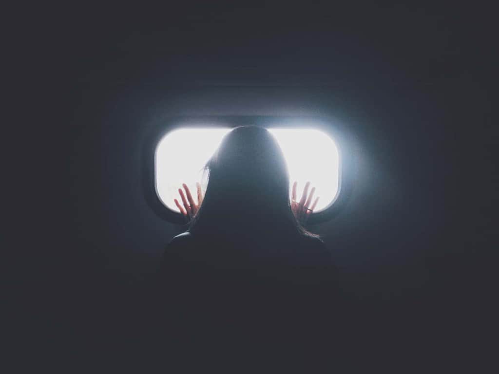 pitch black image with a woman standing and looking out what appears to be a window with daylight outside