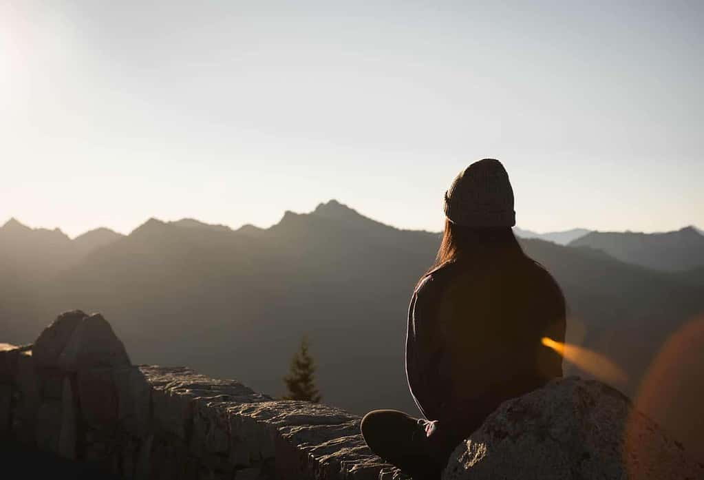 woman sitting on a mountain terrain looking at a beautiful mountain scenary